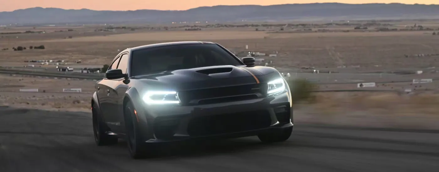 A black 2023 Dodge Charger Scat Pack Widebody driving to a Dodge dealer on an empty road.