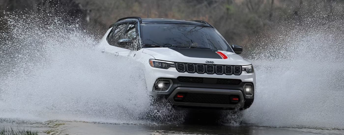 A white 2024 Jeep Compass TrailHawk is shown from the front while driving through water.