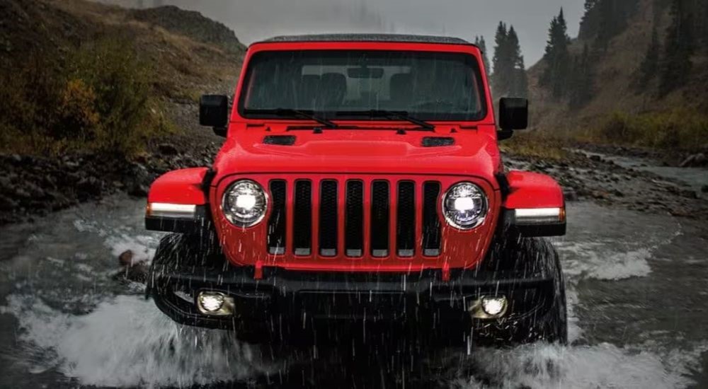 A red 2024 Jeep Wrangler is shown from the front while driving through rain.