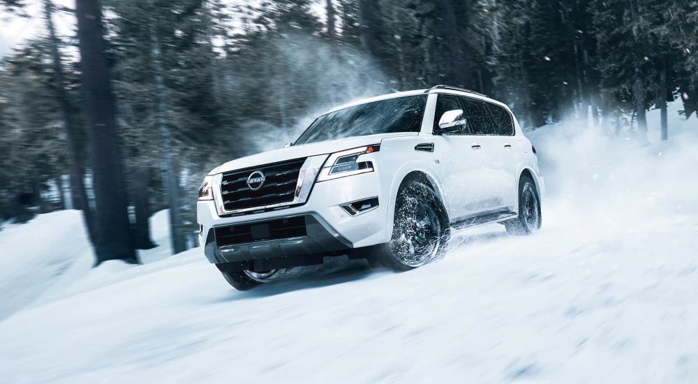 A white 2023 Nissan Armada driving through a snowy forest.