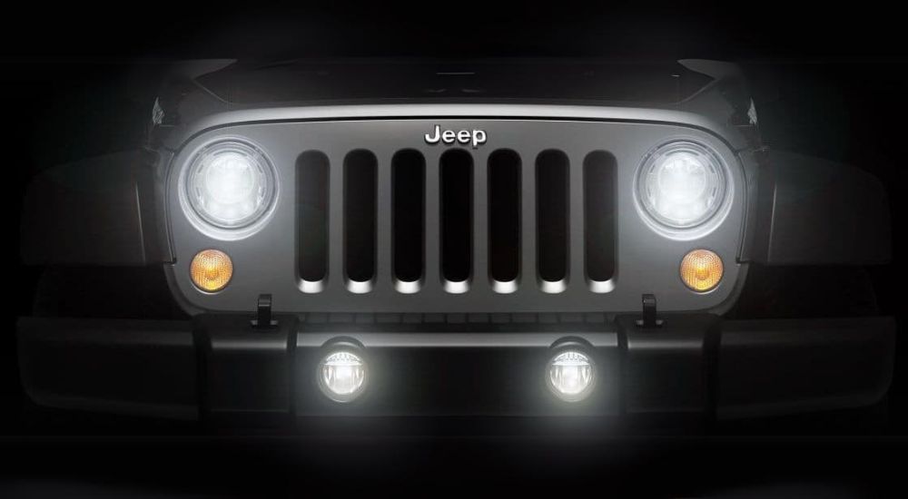 The illuminated headlights are shown on a silver 2017 Jeep Wrangler. 
