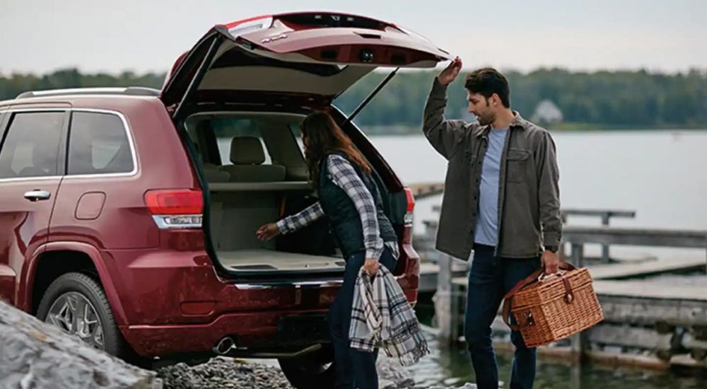 A couple is shown with a picnic basket near a red 2020 Jeep Grand Cherokee.