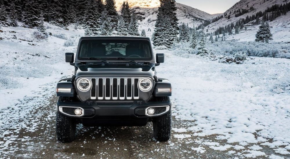 Front angle view of a black 2024 Jeep Wrangler parked off-road on a snowy trail.