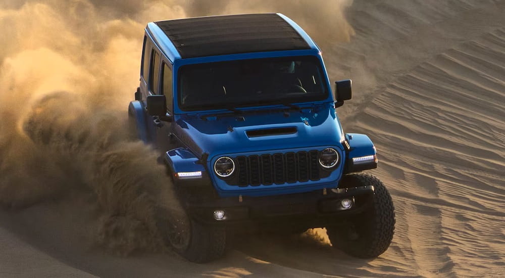 A blue 2024 Jeep Wrangler driving down a dune.