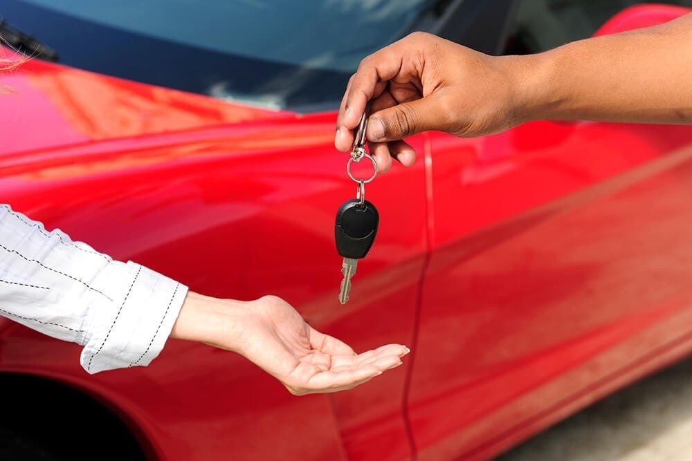 image of someone handing a key to another person in front of a red car