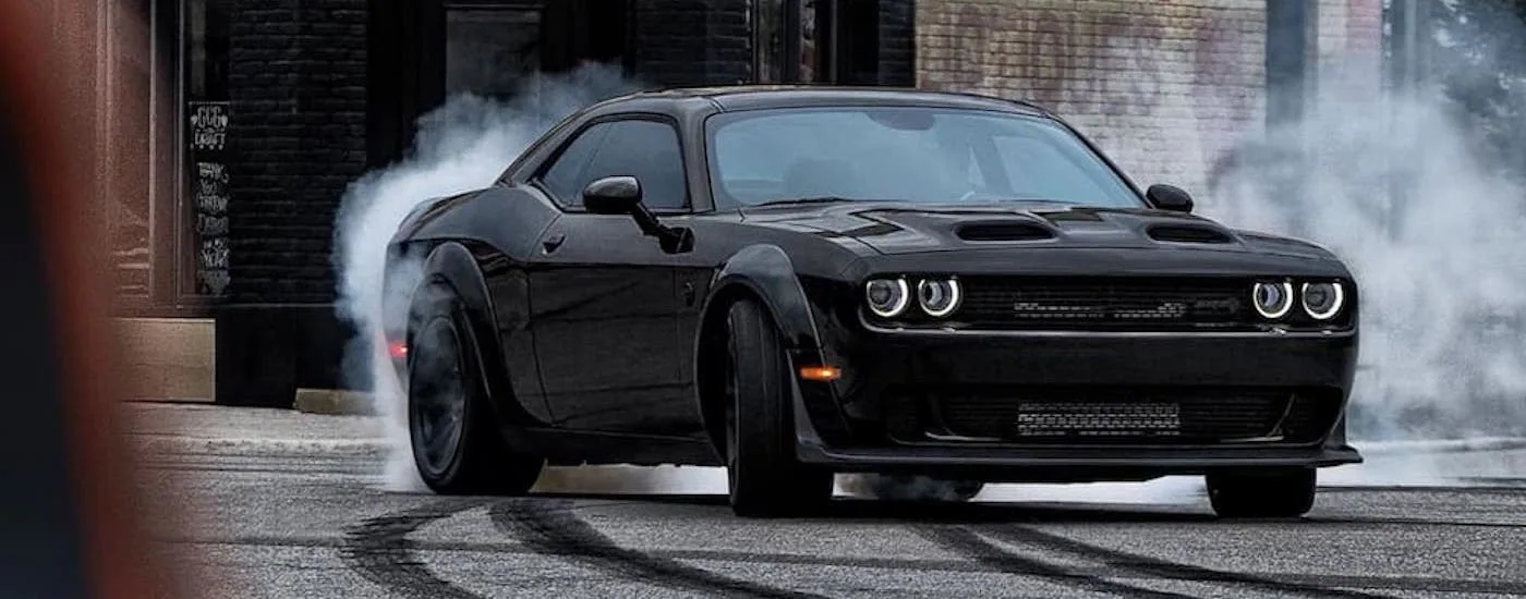 A black 2023 Dodge Challenger Hellcat Widebody Redeye spinning its wheels on pavement.