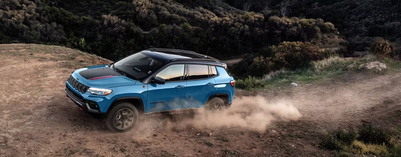 A blue 2025 Jeep Compass Trailhawk is shown from the side while off-road.