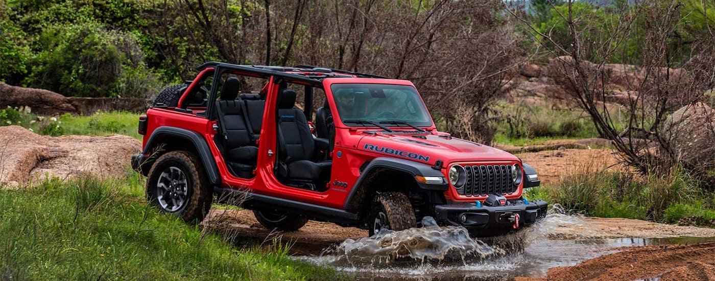 Red 2025 Jeep Wrangler driving over a shallow puddle.