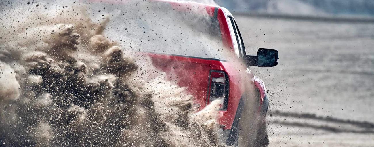 Rear of a red 2024 Ram 1500 driving through a dust cloud.
