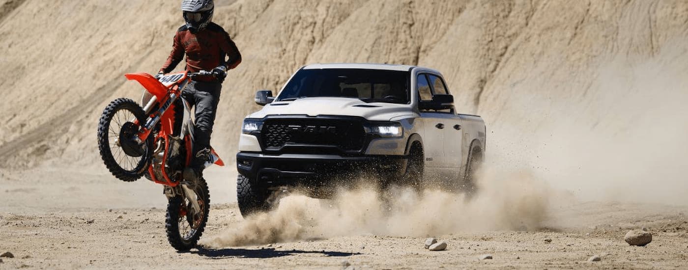 A white 2025 Ram 1500 Rebel driving behind a dirtbike.